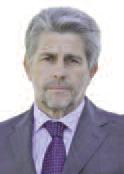 Un uomo di mezza età con capelli grigi e barba corta, che indossa un abito grigio, camicia bianca e cravatta viola, si trova su uno sfondo bianco.